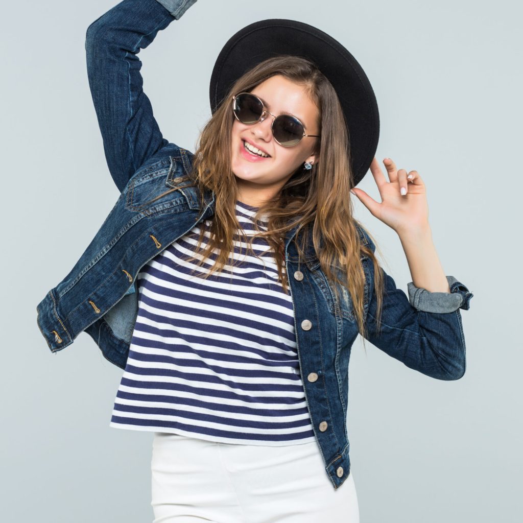 Young woman in a black hat is dancing on white background